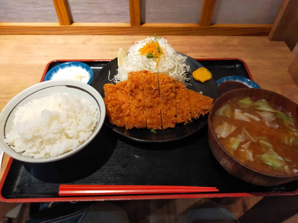 自分 日本語に訳して Copilot トンカツ定食、大盛ご飯付き、美味しい満足感のある一品ですね。栄養バランスを取るには、たっぷりのキャベツを添えて食物繊維を摂り、味噌汁で栄養価をアップするのも良いでしょう。玄米に変えると全粒穀物の摂取量も増えますよ。美味しく召し上がれ！