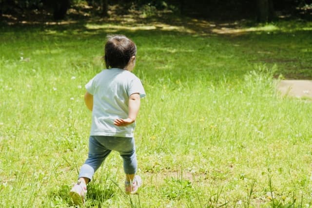 草原を元気に駆け回る小さな子ども。つわりのつらい時期を乗り越えた先に待つ、子どもの成長と幸せな日々を感じさせるイメージ。