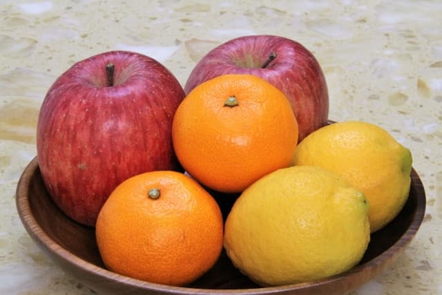 木の器に盛られたりんご、みかん、レモン。つわり中でも食べやすい果物として、少量ずつ摂取するのに適している。酸味やさっぱりした味が食欲を刺激し、吐きづわり・においづわりの対策にもなる。
